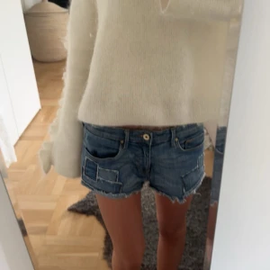jeansshorts med patchdown - Snygga blå jeansshorts med låg midja och råa, fransiga kanter. Shortsen har coola patch-detaljer på båda sidor och klassisk femficksdesign. Perfekta för sommardagar när du vill ha en avslappnad och trendig look.