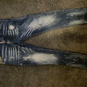 Dsquared2 skinny jeans med färgstänk - Snygga blå skinny jeans från Dsquared2 med coola färgstänk och slitningar. Jeansen har en tight passform, klassisk femficksdesign och tydliga slitdetaljer framtill och baktill. Perfekta för dig som gillar streetstyle och vill sticka ut.