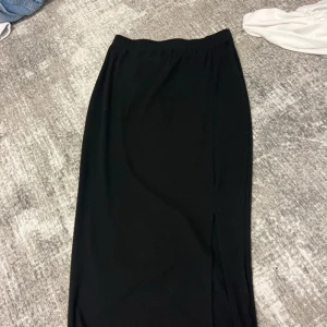 Svart långkjol med slits från SHEIN - Svart långkjol från SHEIN med enkel och clean design. Kjolen har en rak passform och en snygg slits på sidan som ger lite edge. Perfekt att styla med sneakers eller boots för en chill look.