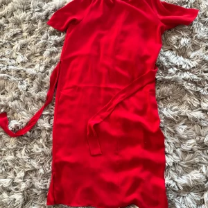 Röd kort klänning från Esprit - Snygg röd midiklänning från Esprit med knytband i midjan och2  slits i sidan. Klänningen har korta ärmar och en enkel, stilren design som ger en snygg och fräsch look. Materialet i hög kvalitet. Den har underklänning. Rekommenderar starkt 