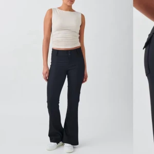 Svarta yk bootcut byxor med fickor - Snygga svarta bootcut byxor med två bakfickor med lock och knapp. Byxorna har en figurnära passform upptill och utsvängda ben. Stängs med knappar framtill. Perfekta för en trendig och stilren look.