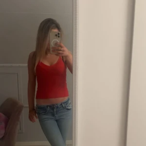 Röd ribbad linnetopp med v-ringning - Säljer en röd ribbad linnetopp med smala axelband och snygg v-ringning. Toppen är croppad och har en figurnära passform som passar perfekt till jeans eller kjol. Materialet är mjukt och stretchigt för en bekväm känsla.