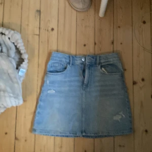 Ljusblå jeanskjol från H&M - Ljusblå jeanskjol från H&M med klassisk femficksdesign, bälteshällor och knappstängning fram. Kjolen har en rak passform och är i mjukt denimtyg, perfekt till sneakers eller boots.