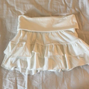 Vit volangkjol med shorts under - Supersöt vit kortkjol med volanger och inbyggda shorts under för extra komfort. Kjolen har bred midjeresår och är gjord i ett mjukt bomullstyg som känns skönt mot huden. Den är helt ny, men passade inte mig❤️