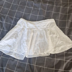Vit kjol - Supersöt vit kortkjol från Gina Tricot med låg midja och små guldiga broderade detaljer. Kjolen är helt ny och aldrig använd, med prislapp kvar. Nypris 230 kr.