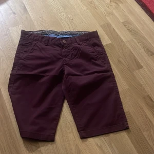 Mörkröda shorts från Pitbull W30 - Snygga mörkröda shorts från Pitbull i klassisk modell med fickor fram och bak. Tillverkade i mjuk bomull med lite stretch för extra komfort. Perfekta för sommardagar när du vill ha en stilren och avslappnad look.