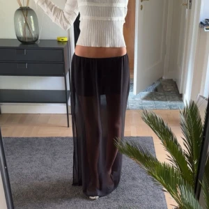 Svart transparent långkjol - Säljer en svart långkjol med transparent yttertyg och kortare underkjol. Kjolen har en rak och flowy passform med resår i midjan, perfekt för en trendig och edgy look. Materialet känns lätt och luftig, vilket ger en snygg layering-effekt. Det är ett gömt resor band så kjolen passar xs-m och för preferens är jag 166