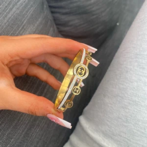 Guldigt armband - Snyggt guldigt armband med glittrande stenar längs ena sidan. Armbandet är stelt och har en elegant, rund form som verkligen sticker ut på handleden. Perfekt accessoar för att lyfta din outfit.