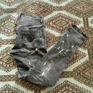 Philipp Plein - Säljer ett par äkta Philipp Plein Biker jeans i grått med mycket slitningar - Storlek 33, Philipp Plein har ribbade partier, röda kontrastsömmar och metallkanpp med logga. Snygg tvätt och tight passform som sitter riktigt bra längs benen. Skick 10/10