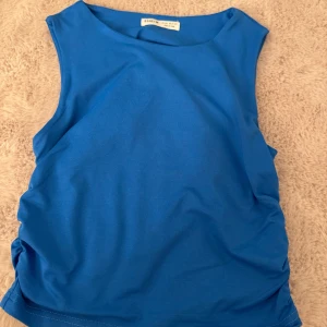 Blå ärmlös topp  - Snygg blå ärmlös topp från SHEIN med rund halsringning och rynkade sidor som ger en cool detalj. Tillverkad i mjuk bomullsmix som känns skön mot huden. Aldrig använd - (passar mig som bär xs/s)