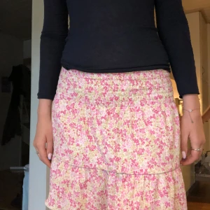 Blommig kjol - Supersöt kort kjol med blommigt mönster i rosa, vitt och lite gult/grönt. Kjolen har volang nertill och smock i midjan för en bekväm passform. Perfekt för varma dagar och ger en fräsch och somrig vibe. Kjolen är från Gina tricot i storlek S! 