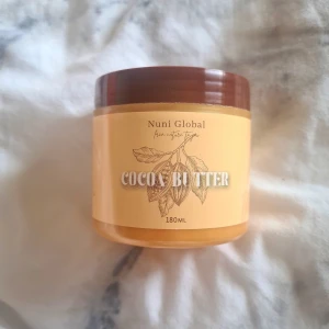 Nuni Global Cocoa Butter 180ml - Helt oöppnad. Cocoa Butter från Nuni Global i en burk på 180ml. Innehåller kakaosmör, vit vaselin, vaselinolja, vitamin E och vatten. Perfekt för att återfukta huden och ge glow. 