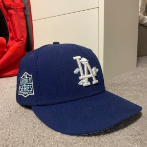 Blå LA Dodgers keps New Era 59FIFTY - En blå Los Angeles Dodgers keps med World Series märke på sidan.  Köpt från neweracap.eu  Kepsen är i nyskick, skärmen är lite lätt böjd men är obruten  Kan samfraktas med andra plagg