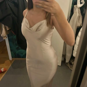 Champagnefärgad långklänning i satin - Supersnygg långklänning i champagnefärgad satin med smala axelband, djup rygg och draperad urringning. Använd en gång!!