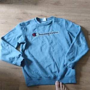 Champion tröja - Säljer en blå sweatshirt från Champion i storlek XL i barnstorlek. Tröjan har rund halsringning, långa ärmar och klassisk Champion-logga broderad på bröstet. Mjuk och skön, perfekt för chill dagar eller när du vill ha en enkel streetstyle-look.