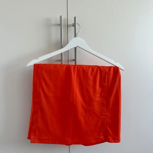 Röd kortkjol från J.Lindeberg - Snygg röd kortkjol från J.Lindeberg i ett slätt och mjukt material. Kjolen har en enkel och stilren design med liten svart logga i midjan. Perfekt för dig som vill sticka ut med färg och gillar sportig vibe.