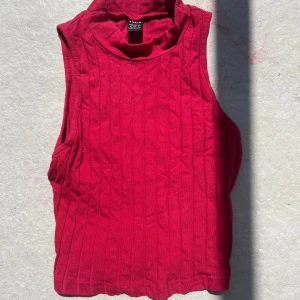 Ribbad röd polotopp från SHEIN - Snygg ribbad polotopp från SHEIN i en djup röd färg. Toppen är ärmlös med hög krage och har en tight passform. Perfekt att styla med jeans eller kjol för en trendig look.