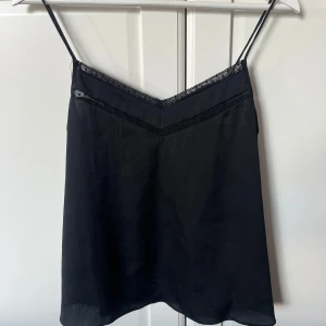 Svart linnetopp med spetsdetaljer - Stilren svart linnetopp med tunna axelband och v-ringning. Toppen har fina spetsdetaljer längs kanten och är i satin. Skriv privat för fler bilder 💞