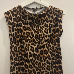 Leopardmönstrad klänning 157 Collection - Snygg kortklänning från 157 Collection med leopardmönster i bruna, svarta och beige toner. Ärmlös modell med rund halsringning, perfekt för dig som vill sticka ut med ett djurmönstrat statement-plagg.