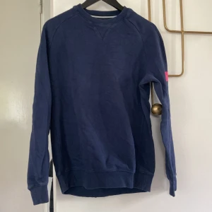 Marinblå sweatshirt från Björn Borg - Snygg marinblå sweatshirt från Björn Borg med rund hals och långa ärmar. Tröjan har en rosa broderad BORG-logga på ena ärmen och är gjord i mjuk bomull. Perfekt för en chill och sportig stil.