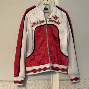 Rosa och vit quiltad träningsjackar - Snygg träningsjacka från Lanshuang i rosa och vitt med coola broderade texter, quiltad framsida och glittriga detaljer. Jackan har dragkedja, långa ärmar med ränder och sportig collegekänsla. Perfekt för dig som vill sticka ut med en trendig look. Storlek L 165/88 samma som träningsbyxorna. Svensk storlek xs/s. Används tillsammans eller var för sig.