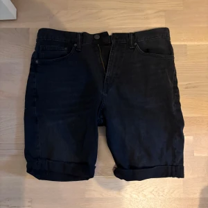 Svarta jeansshorts med upprullad kant - Snygga svarta jeansshorts med klassisk   upprullad kant nedtill (man kan rulla upp dom!). Perfekta för en chill sommarlook och lätta att matcha med allt. Stängs med dragkedja och knapp i midjan. Storlek: 33