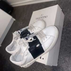 Valentino Garavani Open sneakers vit/svart - Snygga Valentino Garavani Open sneakers i vitt skinn med bred svart läderdetalj över mitten. Jag fick de i min födelsedag jag vill sälja de då jag har slutat använda de.