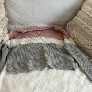 Randig stickad tröja från H&M - Supermysig stickad tröja från H&M med breda ränder i grått, vitt och ljusrosa. Tröjan har lång ärm, ribbad struktur och en relaxed fit. Perfekt för lager på lager under kyliga dagar.