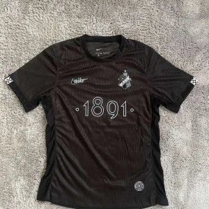 Svart AIK fotbollströja Nike M - AIK fotbollströja från Nike i svart med trycket '1891' på bröstet och klubbmärke. Tillverkad i 100% polyester med Dri-Fit ADV-teknologi för bästa komfort. Slim fit-modell med korta ärmar och diskreta ränder i materialet. Snygga detaljer som rutmönster på ärmslut.