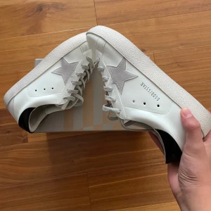 Golden Goose sneakers - Golden Goose sneakers Storlek 43 Vit med grå stjärndetalj och svart häl Helt nya – aldrig använda  Stilrena och helt nya sneakers från Golden Goose – aldrig använda. Perfekta för sommaren tack vare den rena designen och lätta känslan. Ikonisk stjärndetalj i mocka och svart kontrast vid hälen. Kommer utan tillbehör men i originalkartong. Svåra att få tag på – perfekt chans att fynda!  Skriv bara om ni vill ha fler bilder