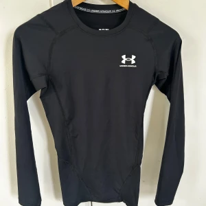 Under Armour kompressionströja träningströja UA XS - Svart långärmad träningströja från Under Armour i storlek XS. Tight passform med vit logga på bröstet och rund halsringning. Tillverkad i stretchigt syntetmaterial som andas, perfekt för intensiva träningspass eller löpning.
