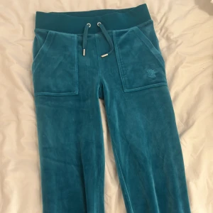 Turkosa mjukisbyxor Juicy Couture XXS - Turkosa mjukisbyxor från Juicy Couture i supermjuk sammet. Byxorna har bred resår i midjan med snörning, stora fickor fram och bak med knappar. Finns en fläck på baksidan på benet men syns knappt när man har på sig. Köpte för 1200kr. Pris går diskutera 