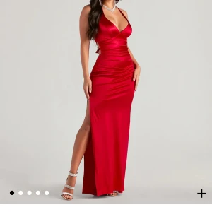 Röd långklänning med slits och snörning - Snygg röd långklänning i satinliknande material med djup v-ringning, smala axelband som korsas i ryggen och knyts i midjan. Klänningen har hög slits på sidan och figurnära passform som framhäver siluetten. Perfekt för bal eller festkväll. Ja bara testa så aldrig riktigt använd!