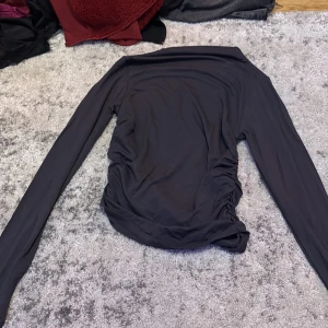 Svart långärmad topp från Gina Tricot Small - Svart långärmad topp från Gina Tricot med snygga rynkade detaljer längs sidorna. Tunn och stretchig i materialet, perfekt för lager-på-lager eller som statement-piece. Enkel att styla till olika looks. Inte använd 