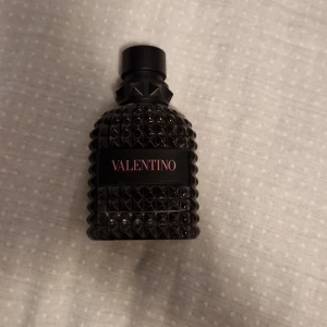 Valentino Born in roma - Snygg parfymflaska från Valentino i svart glas med nitar och mönstrad yta. Flaskan har en svart etikett med rosa text och ett coolt V-logo på korken. Perfekt för dig som gillar lyxiga och stilrena detaljer på parfymhyllan. Cirka 20ml kvar