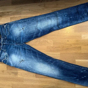 Replay jeans - Snygga blå jeans från replay med slitna detaljer och ljusa partier på låren och knäna. Jeansen har klassisk femficksdesign, röda sömmar och en cool tvättad look. Perfekta för dig som gillar en avslappnad och trendig stil.