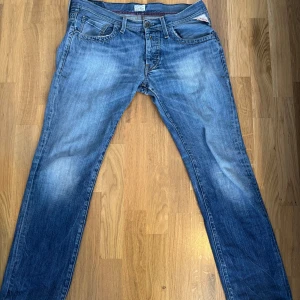 Replay jeans - Säljer ett par klassiska blå jeans från Replay med snyggt slitna detaljer och raka ben. Jeansen har fem fickor, orange sömmar och en tydlig Replay-patch bak i midjan. Perfekta för dig som gillar en tidlös och avslappnad look.