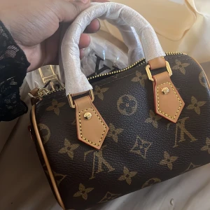  handväska - Säljer en handväska i klassiskt monogrammönster. Väskan är brun med beige detaljer, guldfärgade metalldelar och dragkedja. Tillverkad i skinn med två handtag och avtagbar axelrem. Perfekt storlek.