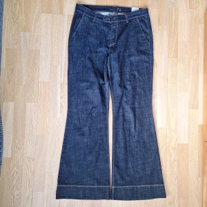 Mörk blåa flare jeans - Snygga blå jeans från MAC. Byxorna har lite utsvängda ben och klassiska fickor fram och dekorativa bakfickor (ej funktionella) med knappdetaljer. Tyget är jeans med lite stretch. 