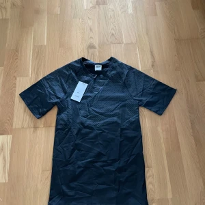 Svart Gymshark t-shirt med mönster - Snygg svart t-shirt från Gymshark med diskret geometriskt mönster över hela tyget. Klassisk rund hals och korta ärmar, perfekt för träning eller chill. Materialet är lätt och andas, vilket gör den grym för aktiva dagar.  ⚠️Denna vara är ej autentisk⚠️