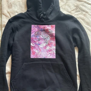 Svart hoodie The Cool Elephant konsttryck - Svart hoodie från The Cool Elephant med en stor, färgstark konstprint i rosa och lila toner framtill. Tröjan har huva med snörning, magficka och lång ärm. Perfekt för dig som gillar unika och kreativa plagg med streetkänsla. I storlek S och i superbra skick! Pris kan diskuteras!