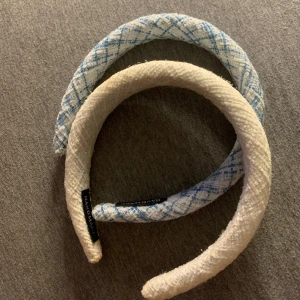Två breda diadem i tweedstil - Säljer två chunky diadem i tweedliknande tyg. Ett är helvitt och det andra är vitt med blått rutmönster. Båda har en mjuk, vadderad känsla och ger en trendig look till håret. Perfekt accessoar för att lyfta din outfit.
