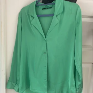 Grön skjorta från Bik Bok i satin - Snygg grön skjorta från Bik Bok i glansigt satinliknande material. Skjortan har klassisk krage, långa ärmar och knäppning framtill. 