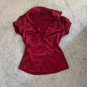 Röd satinskjorta från Gina, strl 34 - röd skjorta i satin från Gina med korta ärmar och markerad krage. Skjortan har knappar framtill och på ärmsluten 💕