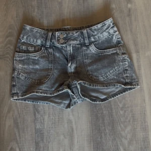 Grå jeansshorts från Lindex - Snygga grå jeansshorts från Lindex med tvättad look och dubbla knappar i midjan. Shortsen har stora framfickor och bakfickor med broderade hjärtan. Perfekta för sommardagar och har en klassisk passform med bälteshällor.