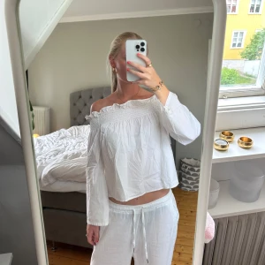 Vit offshoulder blus - Säljer en luftig vit blus med offshoulder och smockad överdel. Blusen har långa ärmar och en lätt rynkad kant upptill. Perfekt till sommaren.