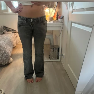 Grå bootcut jeans med detaljer - Säljer ett par grå jeans med bootcut-modell och snygga detaljer på bakfickorna. Jeansen har låg midja och klassisk femficksdesign. Materialet är mjukt denim och passformen är normal. Perfekta för dig som gillar en avslappnad men ändå trendig look.