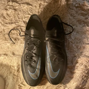 Nike fotbollsskor - Snygga svarta Nike fotbollsskor med blå detaljer och snörning. Modellen phantom GT.