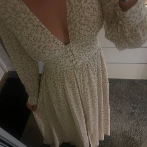 Adoore klänning - Supersöt långklänning från Adoore med ljus botten och små gula blommor. Djup v-ringning, långa ärmar och markerad midja. Perfekt flowy passform och romantisk look. Materialet känns lätt och luftigt.