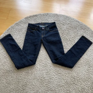 Mörkblå slim fit  jeans från Nudie Jeans - Snygga mörkblå slim fit jeans från Nudie Jeans med klassiska orange sömmar  och ikonisk bakficka med vågig brodyr. Modellen har normal midja och är tillverkad i stretchig bomullsdenim för en bra passform. Perfekta till sneakers eller boots.